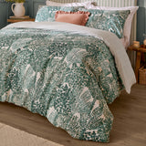 Green Topiary Reversible Botanical Duvet Cover Set with fern print on a bedroom bed, styled with matching pillowcases and a pink cushion, striped reverse edge visible.