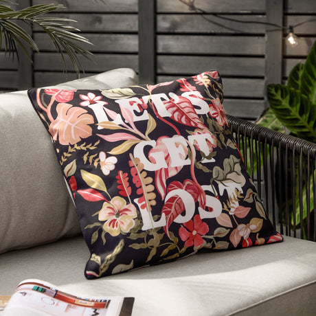 Square black outdoor cushion with tropical floral print in coral, pink and olive tones, featuring bold white "Let's Get Lost" text, shown on an outdoor sofa.