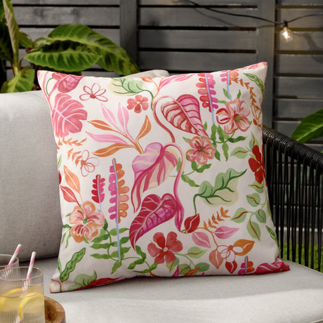 Tropical Bloom Reversible Polyester Cushion in natural cream, featuring a hand-illustrated tropical leaf and floral print in pink, coral and green, shown on an outdoor sofa.