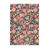 Tropical Bloom rectangular rug in polyester with a dense tropical floral print of coral, blush and apricot blooms and green foliage on a charcoal-black ground, shown on a plain white background.