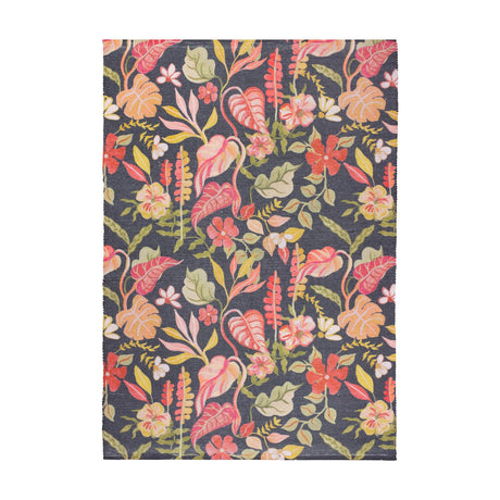 Tropical Bloom rectangular rug in polyester with a dense tropical floral print of coral, blush and apricot blooms and green foliage on a charcoal-black ground, shown on a plain white background.