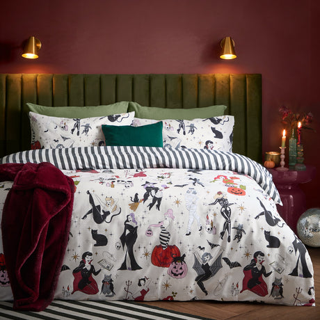 Trick or Treat reversible duvet cover set on a bed with Halloween-print witches, skeletons and pumpkins, paired with black and white striped pillowcases in a dark red bedroom.