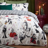 Trick or Treat reversible duvet cover set on a bed, cream side showing Halloween witches, skeletons, mummies and pumpkins, paired with black and white striped pillowcases in a bedroom setting.