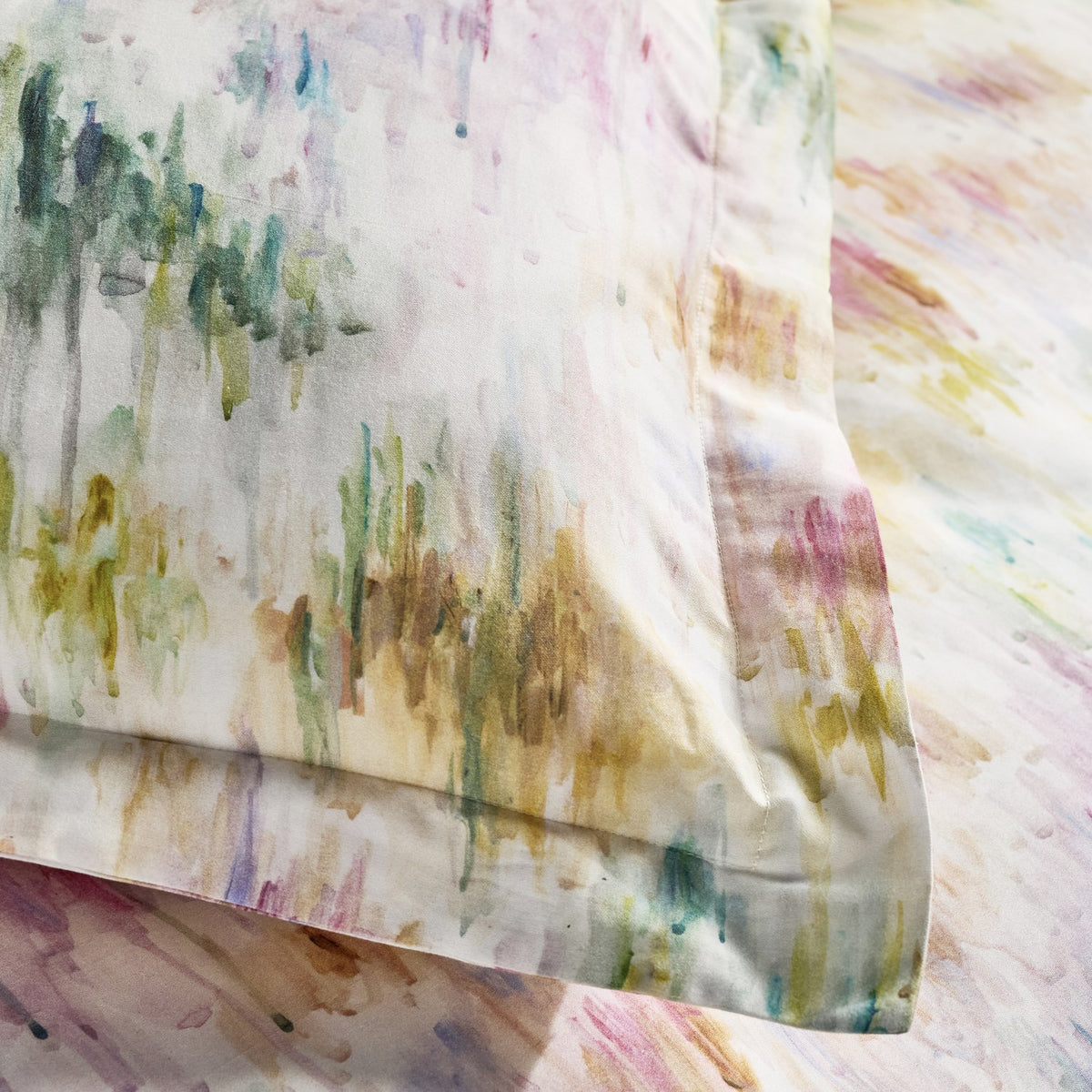 Close-up of the Trueno cotton duvet cover set showing an abstract watercolour print in pink, purple, green, gold and teal on a cream ground, with pillowcase edge and flat sheet visible.