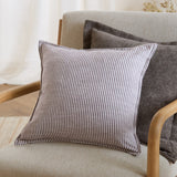 Truro Striped Cotton Cushion in chocolate brown and off-white pinstripe, square shape with piped edge, shown on a light upholstered armchair with grey cushions behind.