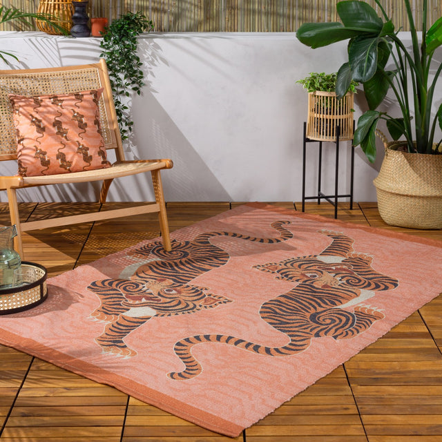 Tibetan Tiger Animal Polyester Rug in coral, flatweave design with two striped tigers, styled on a wooden deck with rattan chair and potted plants.