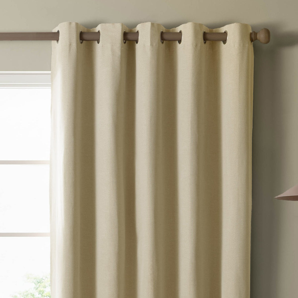 Blackout eyelet curtain panel in custard cream woven fabric, hung on a wooden pole with metal grommets, shown against a window in a neutral-toned room.