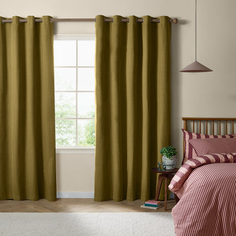 Olive green eyelet blackout curtains in plain woven fabric hung on a wooden pole beside a bedroom window, styled with a wood-framed bed and pink striped bedding.