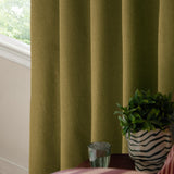 Forest green woven eyelet blackout curtains hanging in soft folds beside a window, styled with a side table, glass tumbler, and striped plant pot.