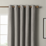 Grey eyelet blackout curtain in textured woven polyester, hung on a wooden pole with metal grommets, shown against a light wall beside a window.