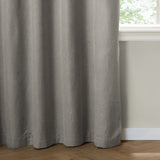 Grey blackout eyelet curtain in textured woven fabric, shown floor-length beside a window with white surround and wooden flooring.