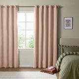 Blush pink eyelet blackout curtains with woven texture hanging beside a window in a bedroom with olive green bedding and a framed print.