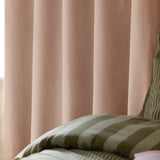 Blush pink woven eyelet blackout curtains hanging in soft folds beside a bed with olive green striped bedding.