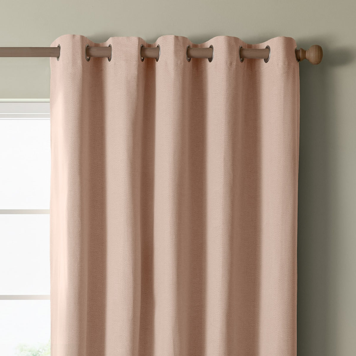 Blush pink eyelet curtain panel with woven texture and metal grommets on a wooden rod, hung against a sage green wall beside a window.