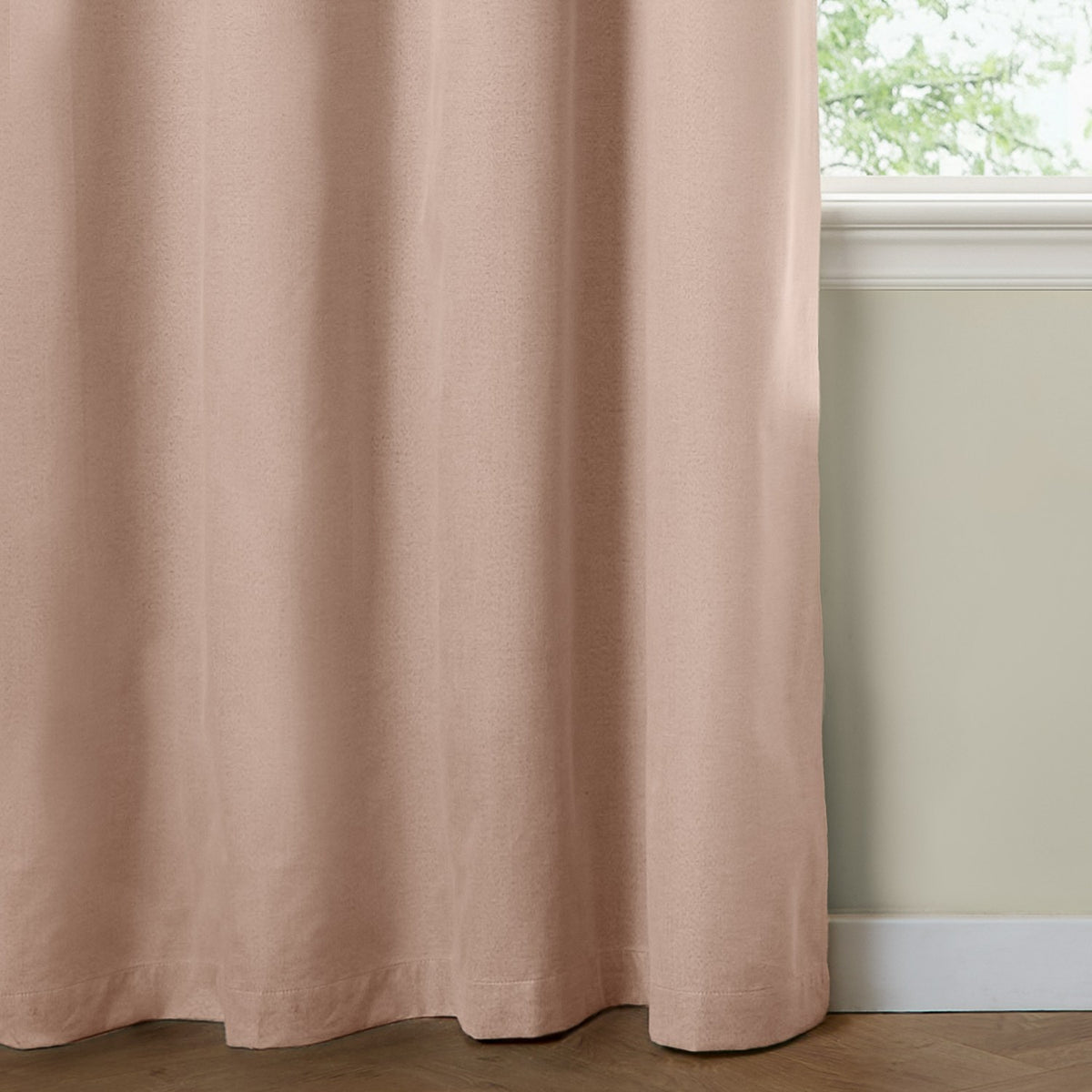Blush pink blackout eyelet curtain in a woven polyester fabric, shown falling in soft folds beside a window with a cream wall and skirting board.