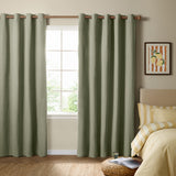 Sage green eyelet blackout curtains in a textured plain weave hang beside a bedroom window, paired with a wooden curtain pole and yellow striped bedding.
