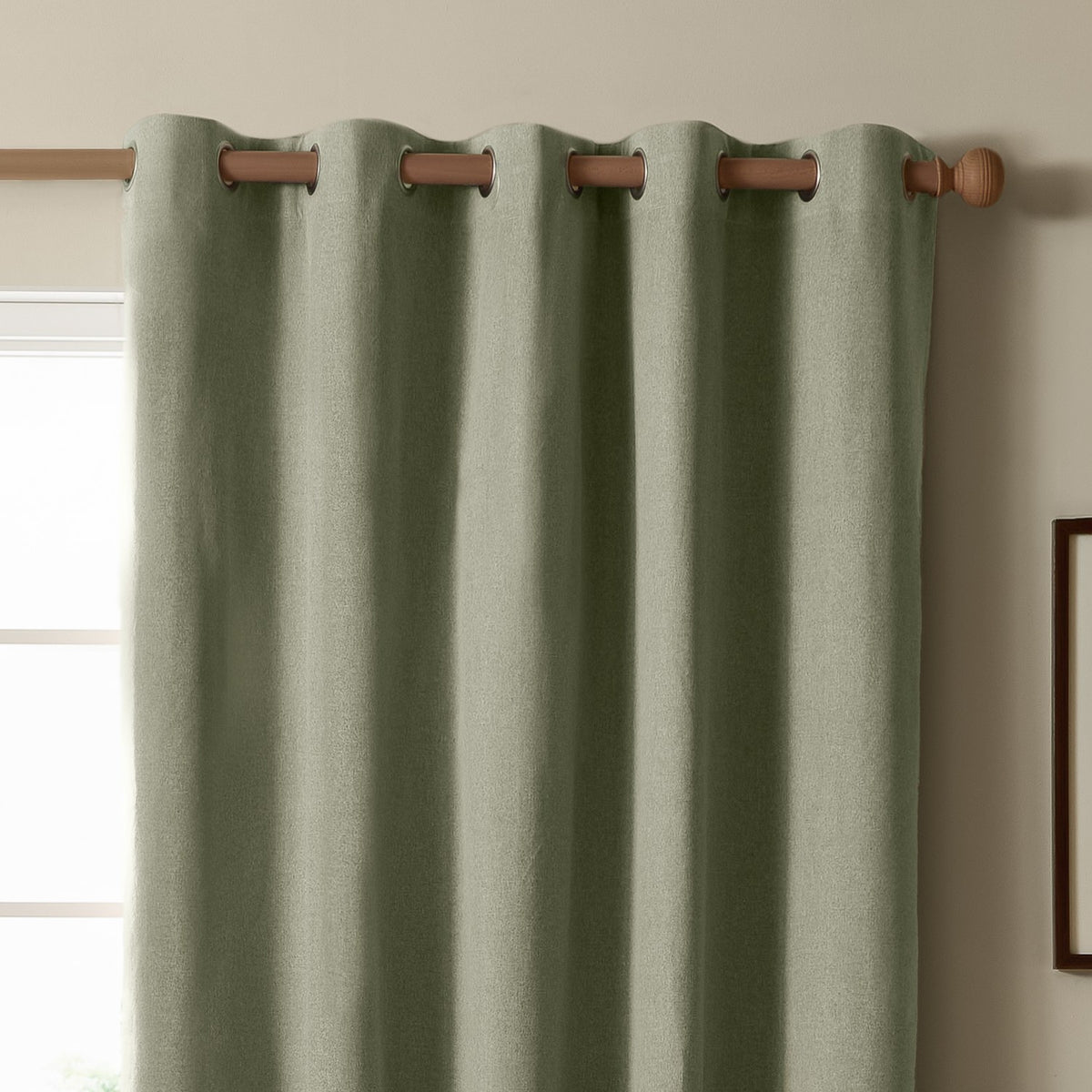 Sage green eyelet blackout curtain in textured plain-weave polyester, hung on a wooden pole with silver-ringed grommets against a neutral wall near a window.
