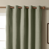 Sage green eyelet blackout curtain in textured plain-weave polyester, hung on a wooden pole with silver-ringed grommets against a neutral wall near a window.