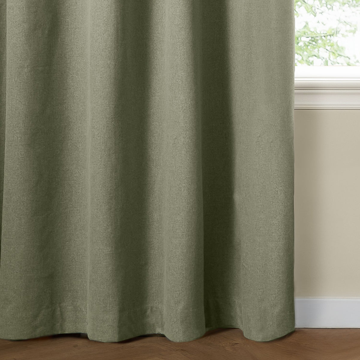 Sage green eyelet blackout curtain in textured plain-weave polyester, shown falling in soft folds beside a window in a room with cream walls.