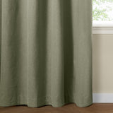 Sage green eyelet blackout curtain in textured plain-weave polyester, shown falling in soft folds beside a window in a room with cream walls.