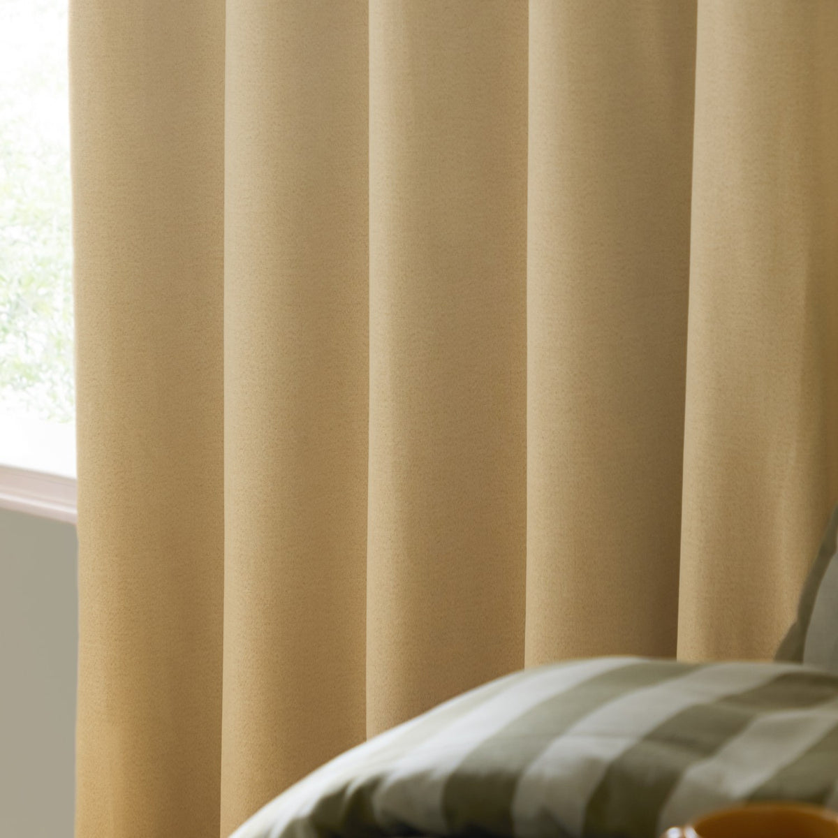 Yellow blackout eyelet curtains in plain woven polyester fabric, shown hanging in soft folds beside a window, with a striped cushion visible in the foreground.
