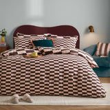 The Ultimate Checkerboard Check Duvet Cover Set in Berry Brownie on a bed with matching pillowcases, pink and brown check pattern, burgundy headboard, and blue armchair in a bedroom setting.