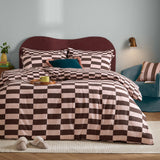 Bedroom scene with The Ultimate Checkerboard duvet cover set in pink and chocolate brown check, styled with matching pillowcases on a bed with a burgundy headboard.