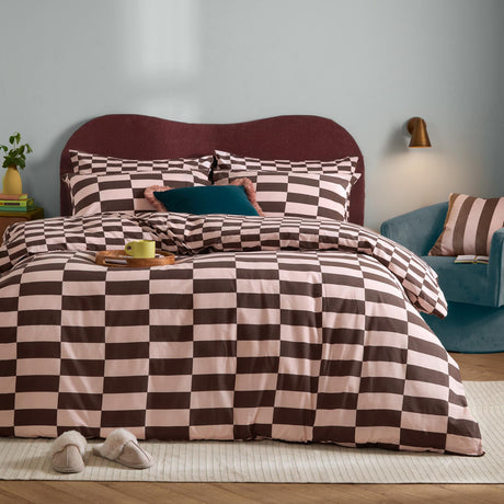 Bedroom scene with The Ultimate Checkerboard duvet cover set in pink and chocolate brown check, styled with matching pillowcases on a bed with a burgundy headboard.