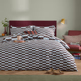 The Ultimate Checkerboard Check Duvet Cover Set in Blueberry Muffin, shown on a bed with a burgundy headboard, featuring a reversible blue and brown checkerboard print with matching pillowcases.