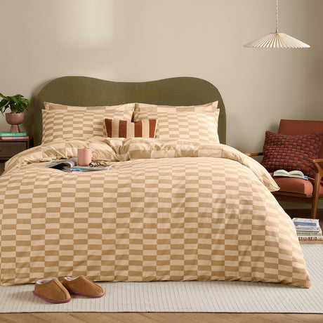 Checkerboard Duvet Cover Set in caramel and latte tones on a bed with matching pillowcases, striped cushion, and green upholstered headboard in a bedroom setting.