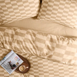 The Ultimate Checkerboard Check Duvet Cover Set in Caramel Latte, shown on a bed with matching pillowcases, striped sheet, and a tray holding coffee, glasses, and a magazine.