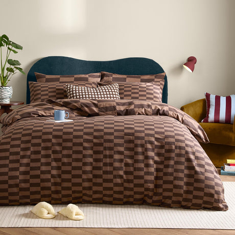The Ultimate Checkerboard Check Duvet Cover Set in Chocolate Truffle brown on a bed with matching pillowcases and cushions, styled in a bedroom with a teal headboard.
