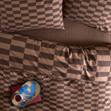 The Ultimate Checkerboard Duvet Cover Set in chocolate truffle brown, shown on a bed with matching pillowcases and a striped fitted sheet beneath.