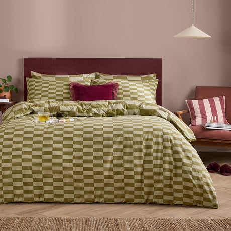 The Ultimate Checkerboard Check Duvet Cover Set in Green Tea, styled on a bed with pillowcases in a bedroom with a burgundy headboard and pink accent chair.