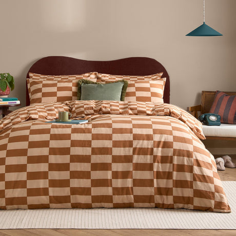 The Ultimate Checkerboard Check Duvet Cover Set in Pumpkin Spice, shown on a bed with matching pillowcases in an orange and sand checkerboard print, styled in a bedroom with a green cushion.