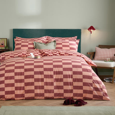 The Ultimate Checkerboard Duvet Cover Set in raspberry smoothie, styled on a bedroom bed with matching pillowcases against a green upholstered headboard.