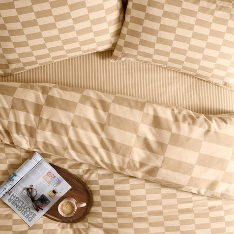 Bedroom scene with The Ultimate Checkerboard Cotton Blend Pillowcase Pair in caramel and cream, reversible checkerboard design, styled with striped duvet, tray, magazine, glasses and a coffee cup.