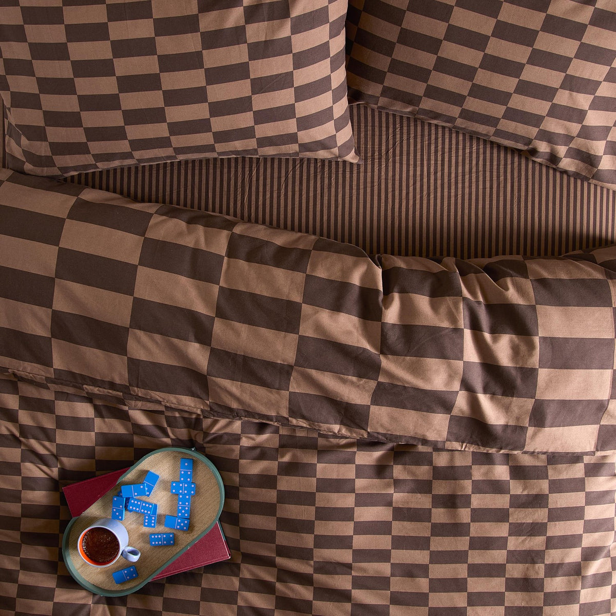Bedroom setting with The Ultimate Checkerboard Cotton Blend Pillowcase Pair in Chocolate Truffle, brown checkerboard bedding and pillowcases styled with a domino tray and coffee cup.