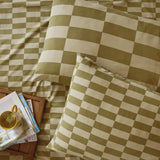 Green and cream checkerboard cotton blend pillowcase pair in Green Tea, shown on a bed with matching duvet, styled with a tray, mug, and magazines.