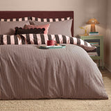 The Ultimate Stripe Reversible Duvet Cover Set in Berry Brownie shown on a bed with narrow and broad brown-and-pink stripe sides, styled with matching pillowcases in a bedroom setting.