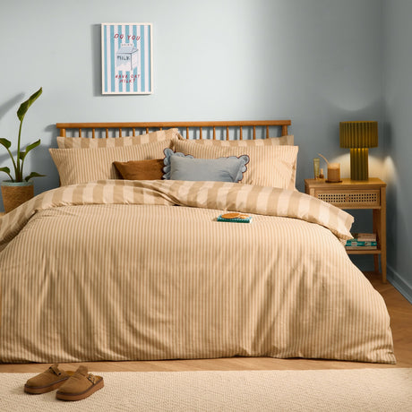 The Ultimate Stripe Reversible Duvet Cover Set in caramel latte on a bed with matching pillowcases and cushions, in a light blue bedroom with wooden headboard.