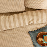 The Ultimate Stripe Reversible Duvet Cover Set in Caramel Latte, shown on a bed with matching pillowcases in beige and cream stripes, styled with a bedside tray.