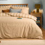 The Ultimate Stripe Reversible Duvet Cover Set in Caramel Latte dressed on a bed with matching pillowcases, styled in a bedroom beside a wooden nightstand and lamp.