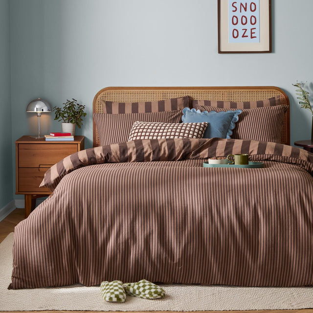 The Ultimate Stripe Reversible Duvet Cover Set in Chocolate Truffle on a bed in a bedroom, with narrow and wide brown-and-caramel stripes, cane headboard, and coordinating pillows.