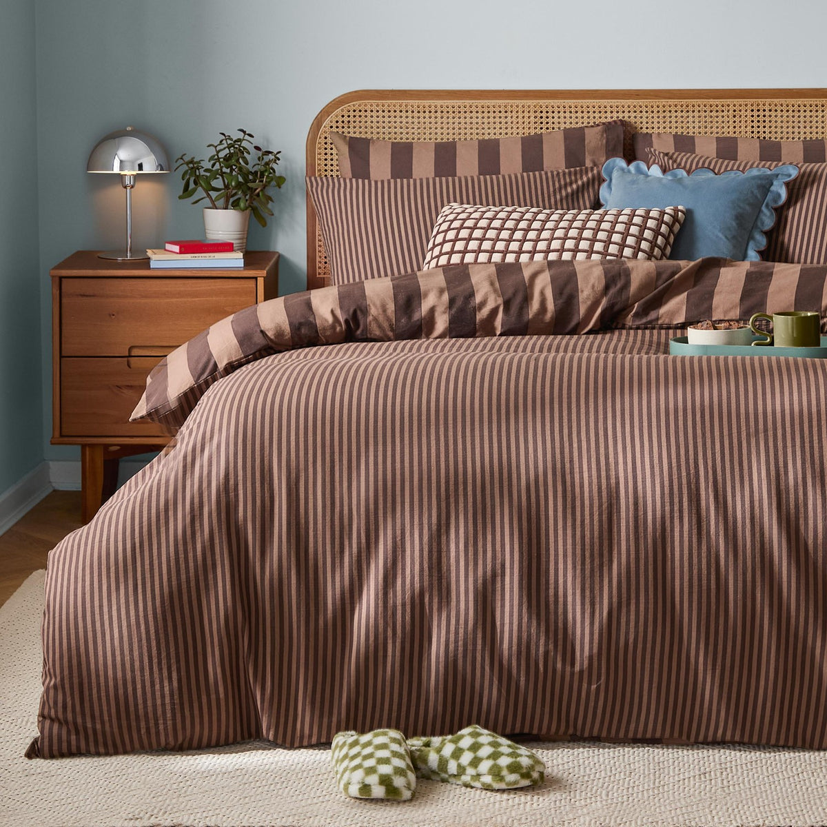 The Ultimate Stripe Reversible Duvet Cover Set in Chocolate Truffle dressed on a bed with pillows, styled in a bedroom with a rattan headboard and wooden nightstand.