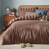The Ultimate Stripe Reversible Duvet Cover Set in Chocolate Truffle dressed on a bed with pillows, styled in a bedroom with a rattan headboard and wooden nightstand.