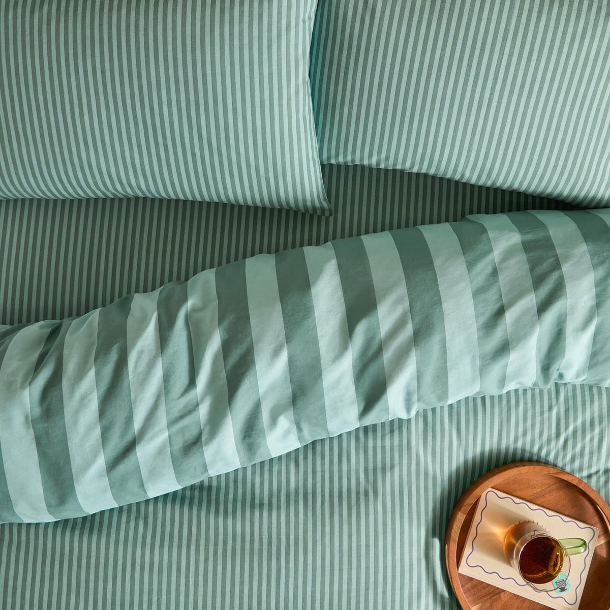 The Ultimate Stripe Reversible Duvet Cover Set in Peppermint, styled on a bed with matching pillowcases, showing both narrow and bold striped sides in green and white cotton blend fabric.