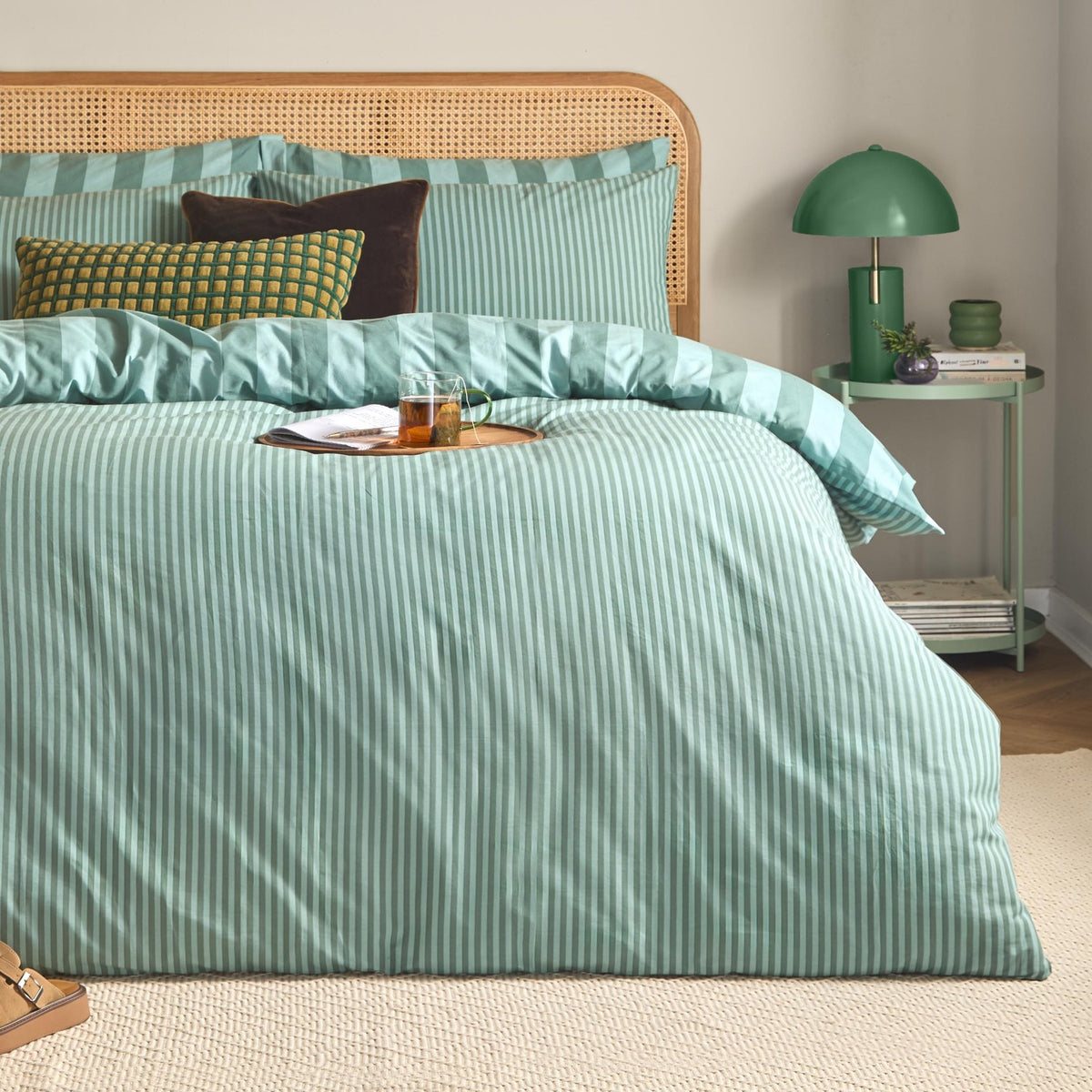 Peppermint green reversible striped duvet cover set with narrow-striped pillows and wide-banded duvet, shown in a bedroom with a rattan headboard and green side table.