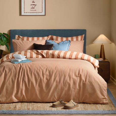 The Ultimate Stripe Reversible Duvet Cover Set in Pumpkin Spice, rust and cream striped cotton blend bedding with matching pillowcases on a bed with a blue upholstered headboard.