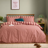 The Ultimate Stripe Reversible Duvet Cover Set in Raspberry Smoothie, styled on a bed with matching pillowcases in pink and blush stripes, in a sage green bedroom.